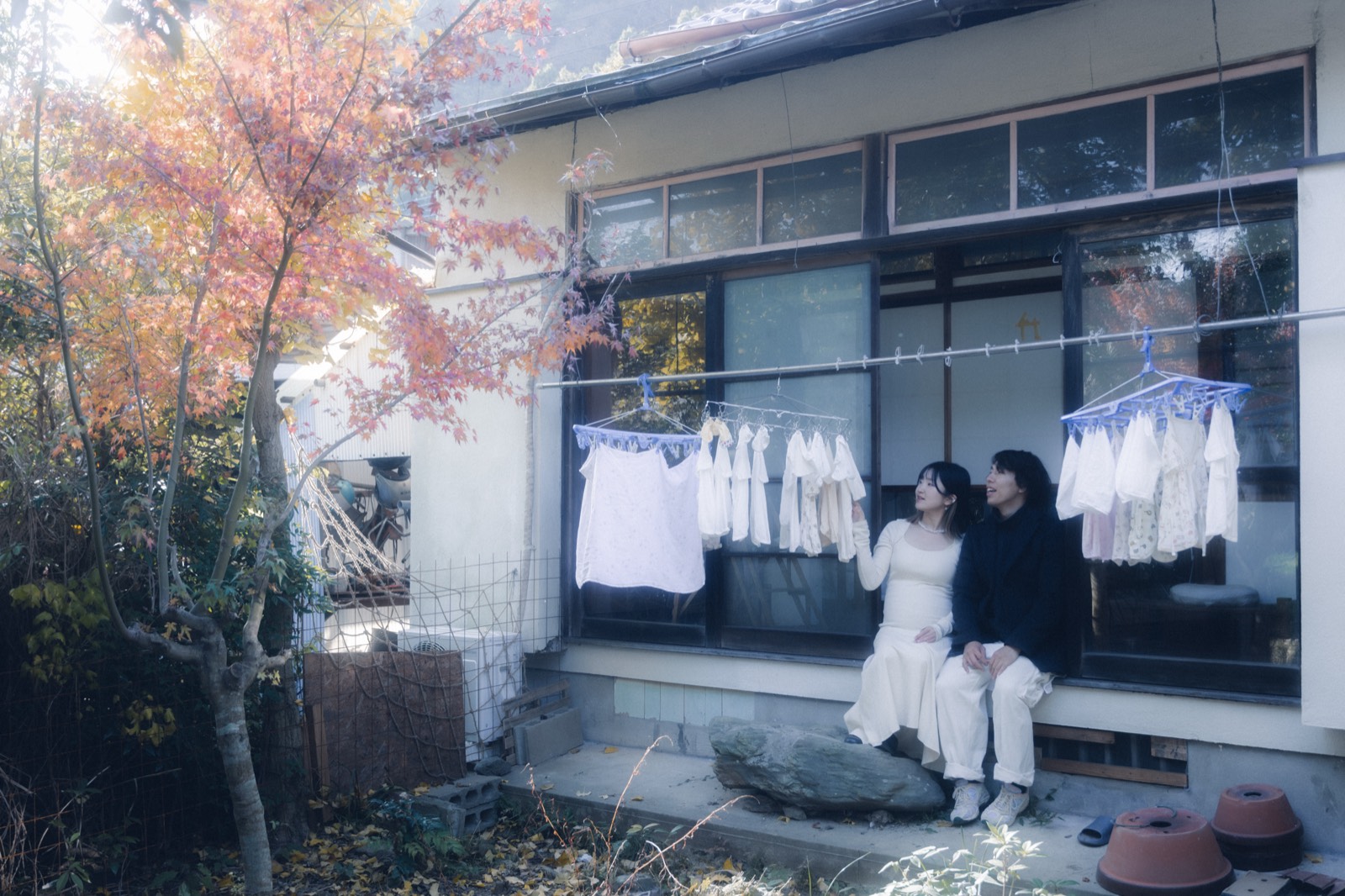 紅葉した木の下、縁側に洗濯物が干された古い家